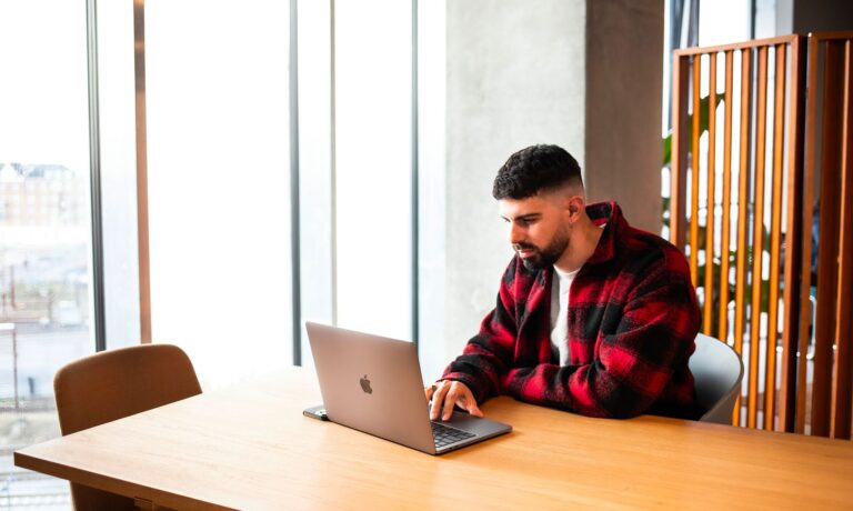 Junge Person plant den Umzug nach Dänemark mit Laptop, Notizen und Checkliste am Schreibtisch