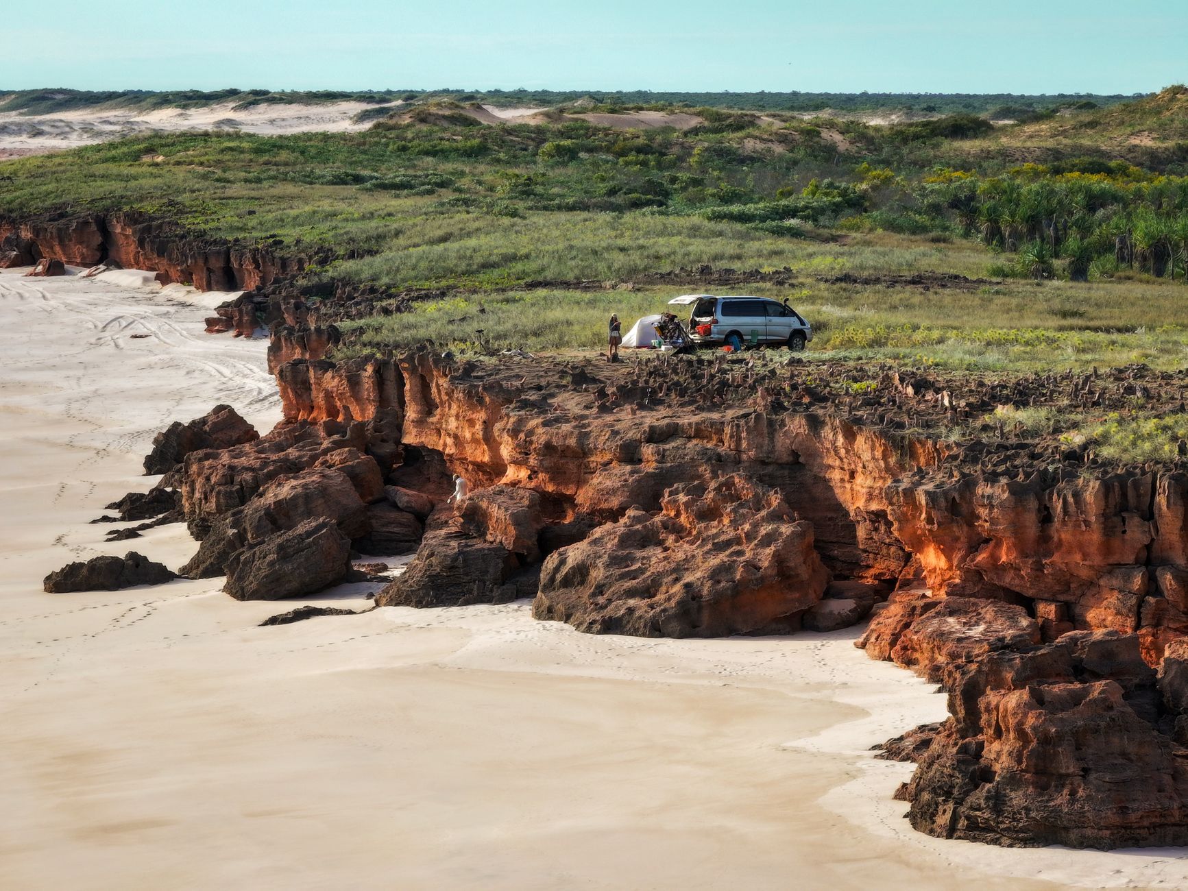 Zwei Backpacker stehen vor ihrem Miet-Camper an einer Küstenstraße in Australien