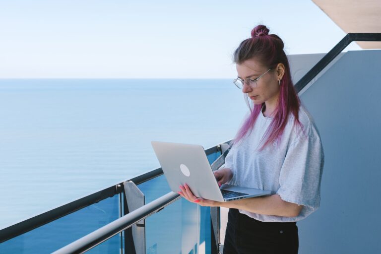 Junge Remote-Workerin sitzt mit Laptop in einem europäischen Straßencafé und verbindet Arbeit mit Reisen